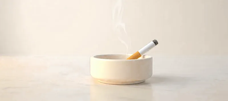 Une cigarette éteinte dans un cendrier en céramique, un filet de fumée.